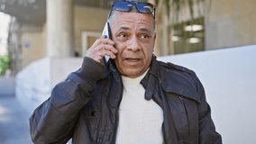 Hispanic man in jacket talking on a smartphone on a sunny city street - Powered by Shutterstock - Get 15% off with code: PIKWIZARD15