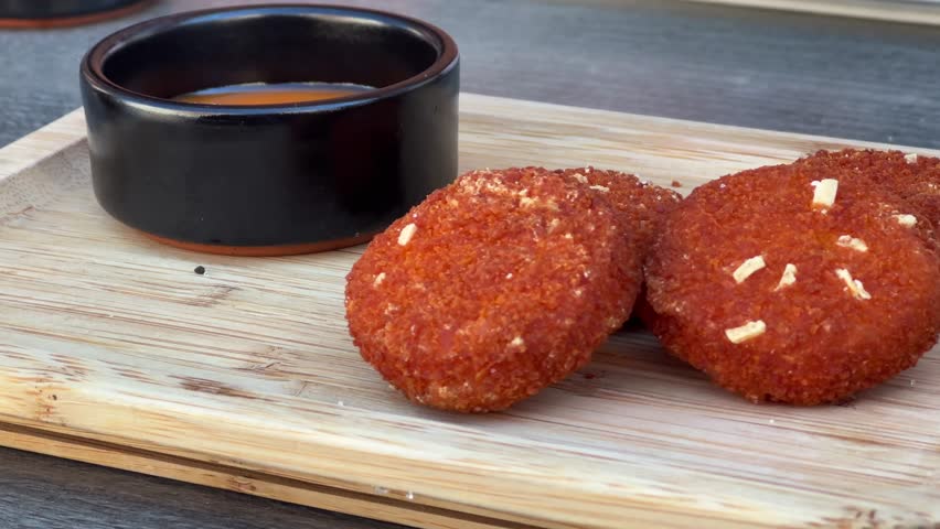 Close-up of crispy fried shrimp cakes garnished with garlic, served on a wooden board with a bowl of dipping sauce.

