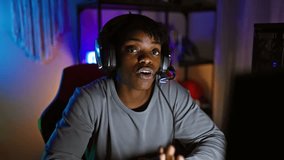 African american woman with dreadlocks wearing headphones in a dark gaming room at night appears cheerful and engaged.