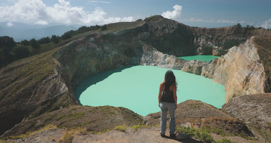Woman looking on volcano mountain crater edge. Volcanic Kelimutu blue crater lake. Travel destination. Beautiful wild landscape. Female tourist on summer vacation. Lifestyle holiday concept. Back view