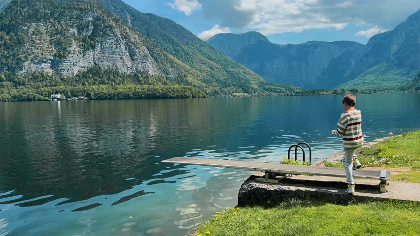 A teenage boy inspects a mountain lake on a sunny day
