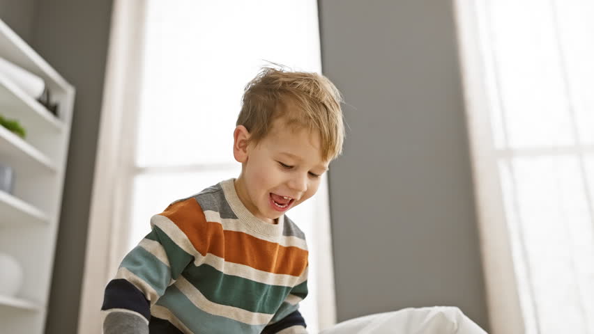 A playful boy entertains himself with a stuffed animal on a cozy bedroom bed, showcasing a moment of pure childhood joy indoors.