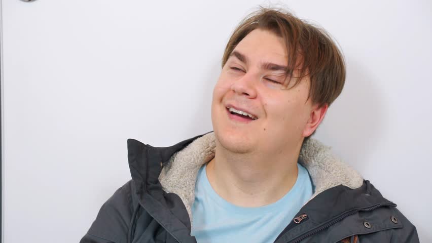 Mentally ill man with weird face expressions against white wall. Male grappling with mental health challenges reflects complexity of emotional state