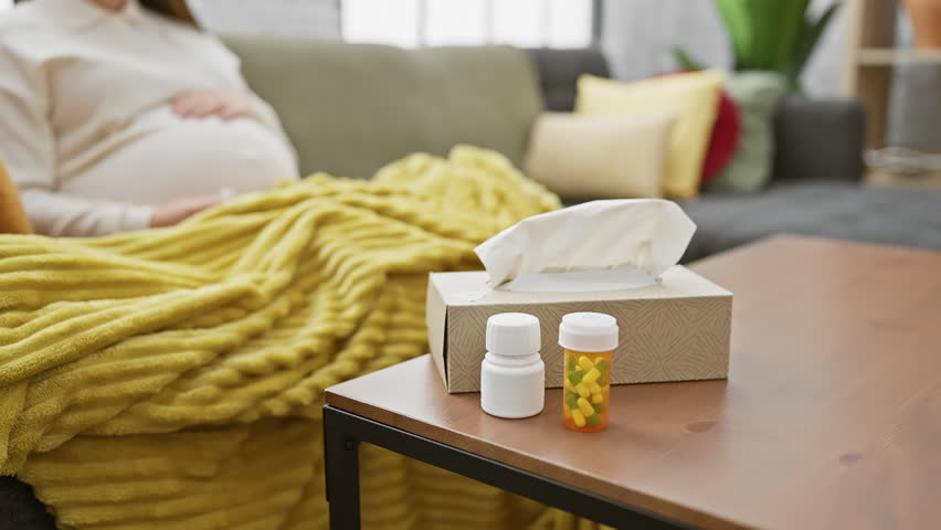 Pregnant woman feeling unwell at home, with medications, in a cozy living room.