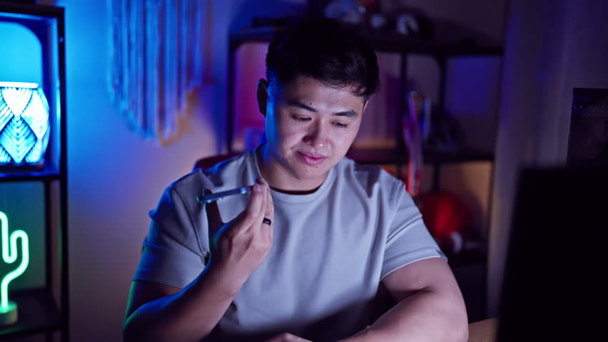 Smiling asian man in a neon-lit room at night, radiating a trendy vibe with tech gadgets and playful lights, exuding cool, modern youth culture.