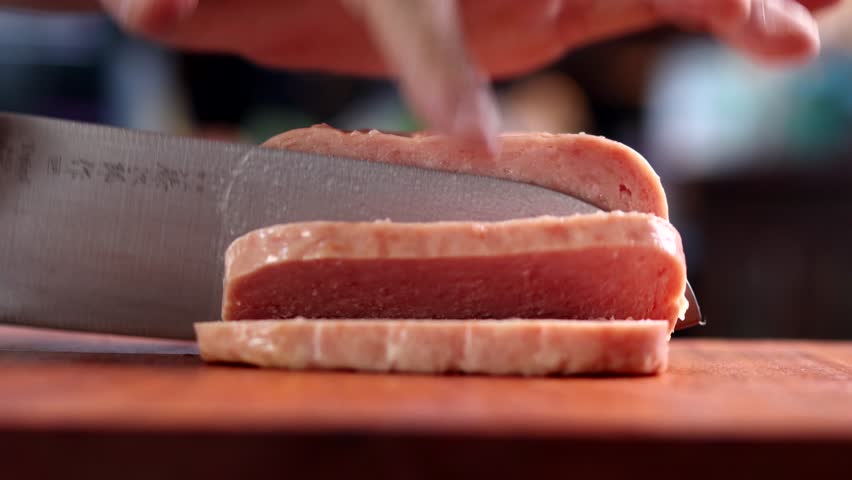 low angle shot of spam being sliced on a wooden cutting board