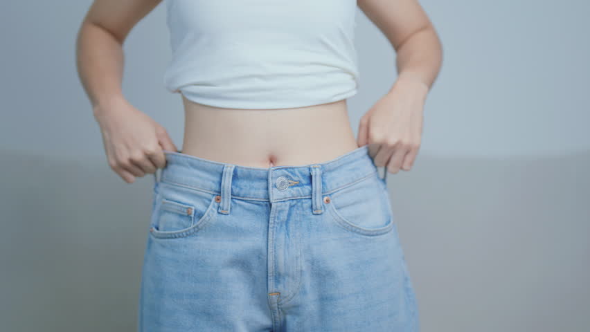 young slim female wearing big or oversize jeans, woman show healthy shape after weight loss. dieting, exercise, body fit and liposuction surgery concept