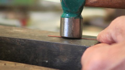 jewlery making: goldsmith banging a metal chord with a green hammer CU
