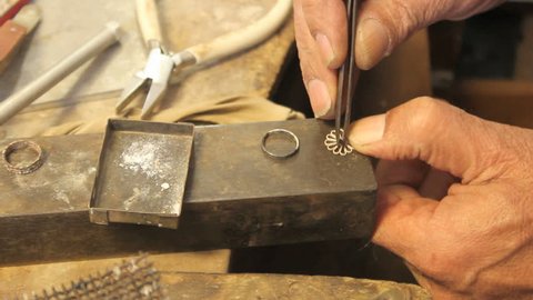 cu on silversmiths hands putting a flower shaped jewelry into a metal ring with tweezers