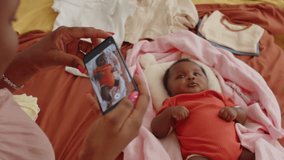 Pan shot of African American woman filming video of baby daughter on smartphone