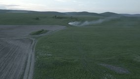 Flat Aerial video. Fairytale place with hills full of green trees and cereals. Birds flying over the hills and country roads at sunset with a place where something burns and smoke comes out