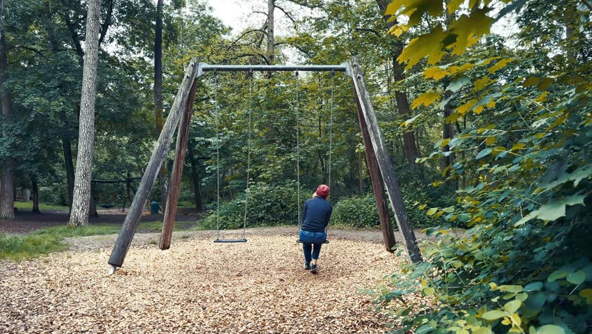 A lonely and sad woman, swinging in a playground. 