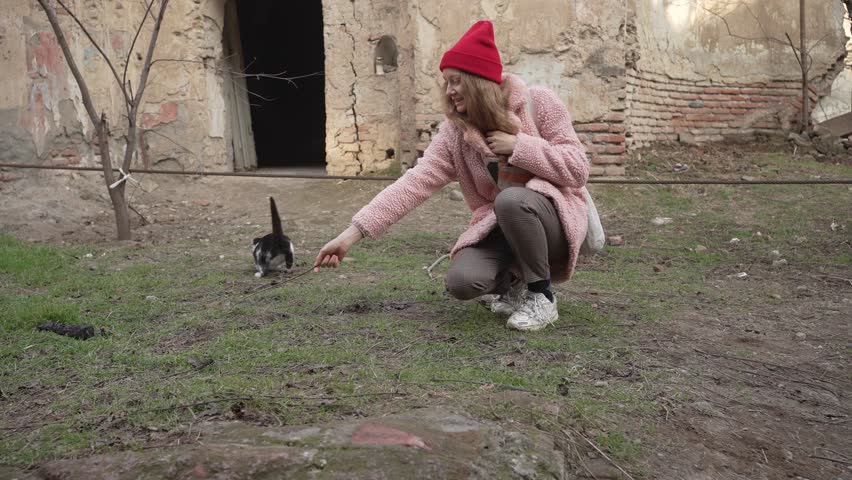 Young woman playfully with stray cat amidst the ruins of old courtyard, showing moment of joy and care.