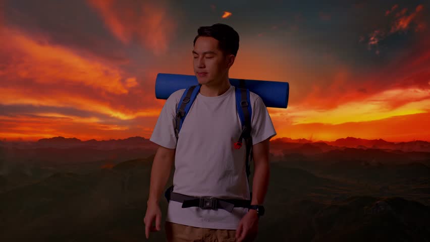 Asian Male Hiker With Mountaineering Backpack Smiling And Pointing To Side While Standing On Top Mountain During Sunset Time