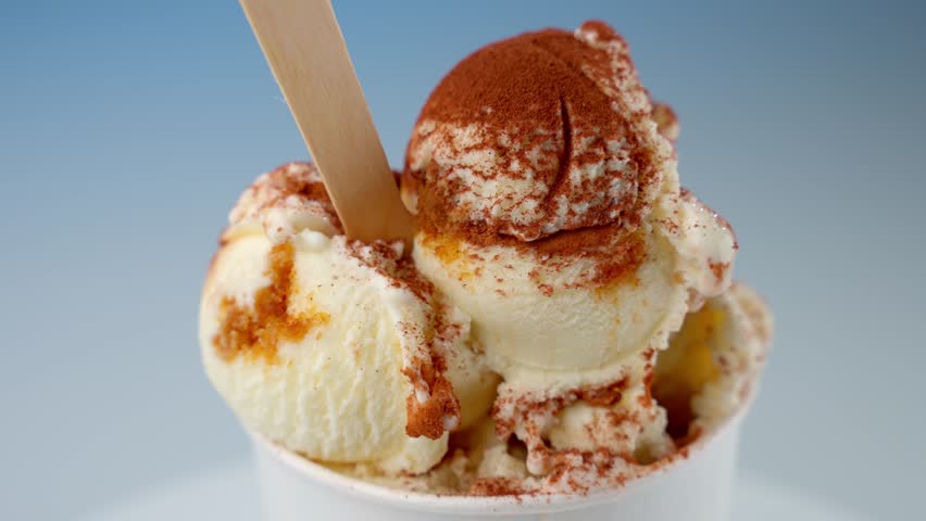 Delicious ice cream with cinnamon powder in cup. Vanilla ice cream sprinkled with cinnamon in paper cup with wooden spoon. Concept Dessert, vanilla, cinnamon