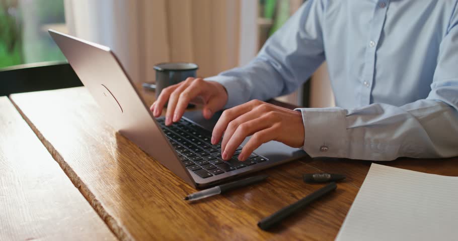 A man uses a laptop sitting at the kitchen table. Close-up of his hands, an unrecognizable person