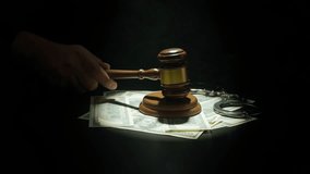 Female at desk with wooden hammer, dark room bright spotlight and smoke. Woman judge in the court room, hand hitting wooden gavel, money and handcuffs laying around, close up shot. - Powered by Shutterstock - Get 15% off with code: PIKWIZARD15