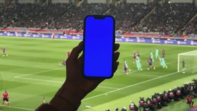 Man watches football at the stadium, holds a phone with a blue screen in his hands. Makes bets on sports. - Powered by Shutterstock - Get 15% off with code: PIKWIZARD15