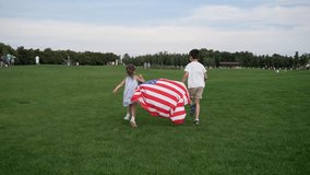 Mixed race boy and girl playing with American flag in a grassy field on 4th July under a clear sky, surrounded by trees. Happy and carefree kids enjoying the leisure outdoors. 4k High res - Powered by Shutterstock - Get 15% off with code: PIKWIZARD15