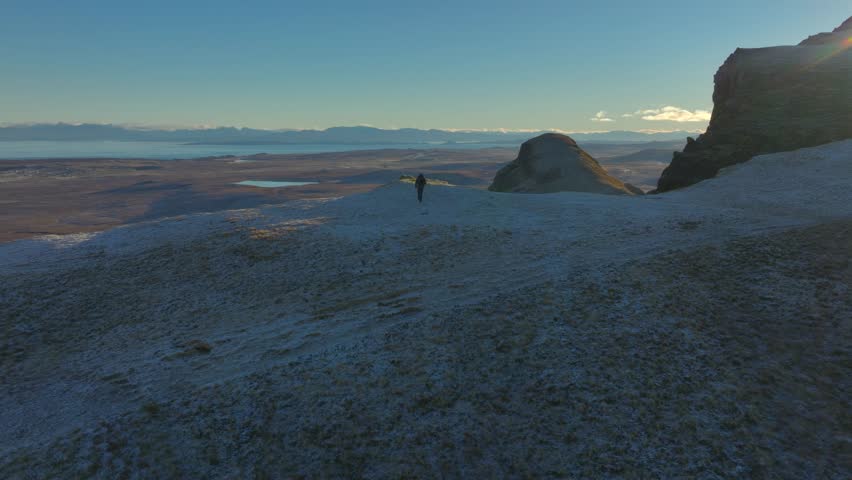 Approaching mountain walker walking to dawn lit frosty cliff edge with far view to mountainous winter horizon. Trotternish Ridge, Isle of Skye, Scotland