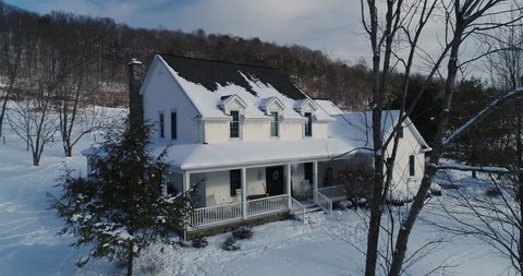 A slow aerial push establishing shot of a typical snow-covered Pennsylvania farmhouse in Winter.	 	