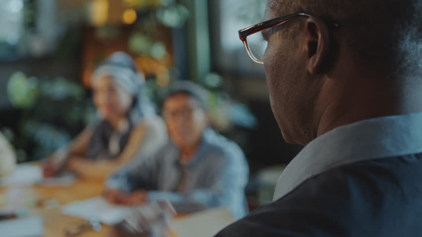 African American professor talking in front of group of diverse adult students sitting around table in classroom and listening attentively during English class in school for immigrants. Rack focus - Powered by Shutterstock - Get 15% off with code: PIKWIZARD15