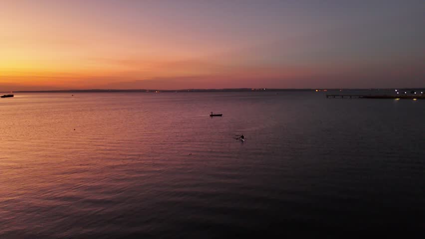 Fisherman in a canoe on the Paraná River with the cityscapes of Posadas at sunset in the background, Argentina
