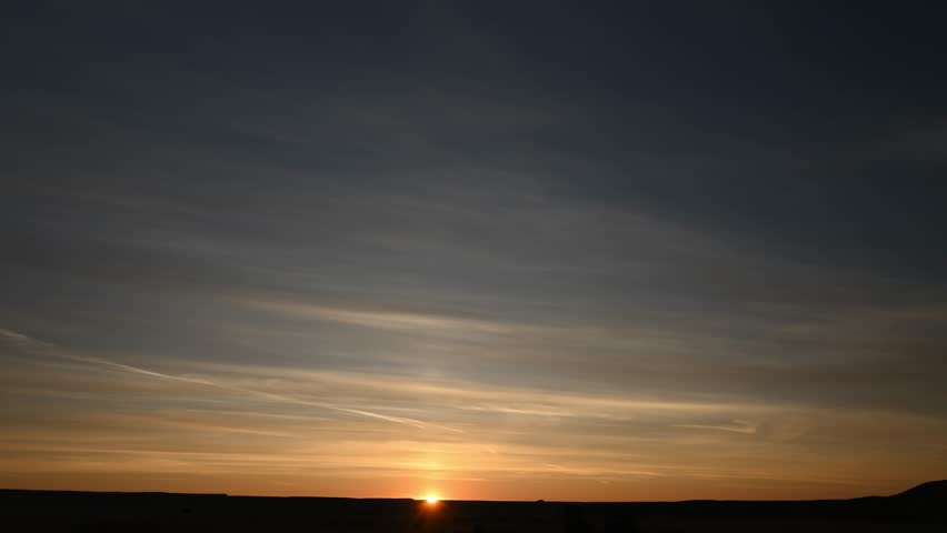 Time lapse of a colorful sunrise with the sun slowly rising above the horizon.  The midground is a flat treeless prairie with small hills.
