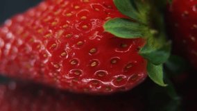Macro detailed video of a pile of strawberries, red strawberry, green leaf, tiny yellow seeds, on a rotating reflection stand, smooth movement. studio lighting glow, 4K