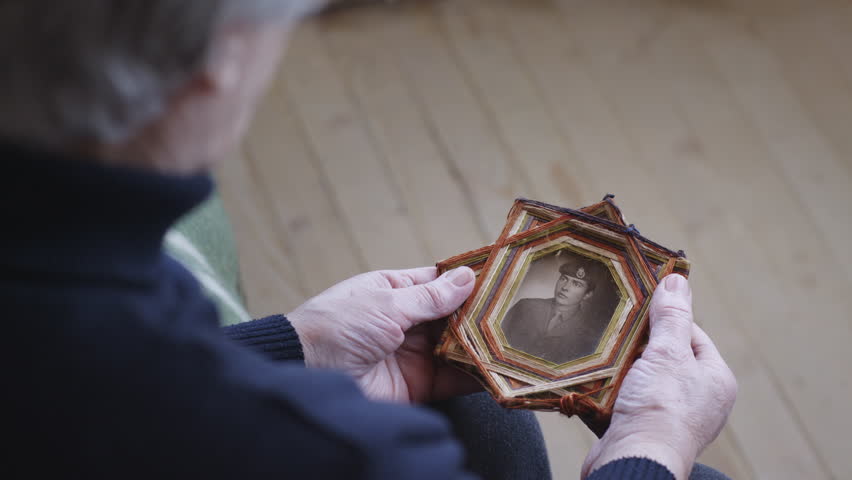 A senior woman cradles an old framed photo of a soldier, capturing a moment of reflection and remembrance. Royalty-Free Stock Footage #3498214249