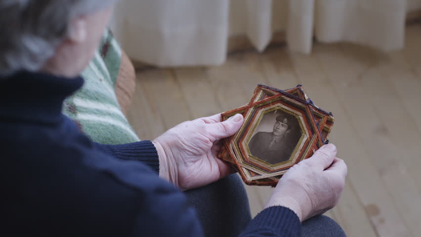 A senior woman cradles an old framed photo of a soldier, capturing a moment of reflection and remembrance. Royalty-Free Stock Footage #3498217677