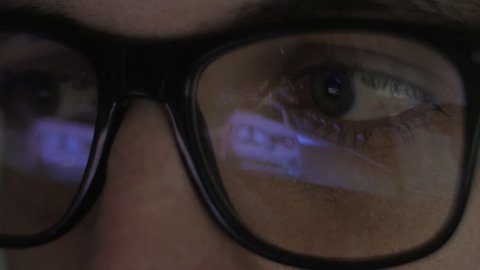 close-up reflection in glasses: Gamer plays a video game on a computer in a dark room