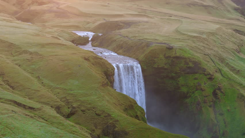 Aerial parallax perspective shows the stunning Skogafoss waterfall dramatically cutting through lush Icelandic hills, embodying the raw, unspoiled beauty of the landscape. at sunrise, Iceland, Skogar 