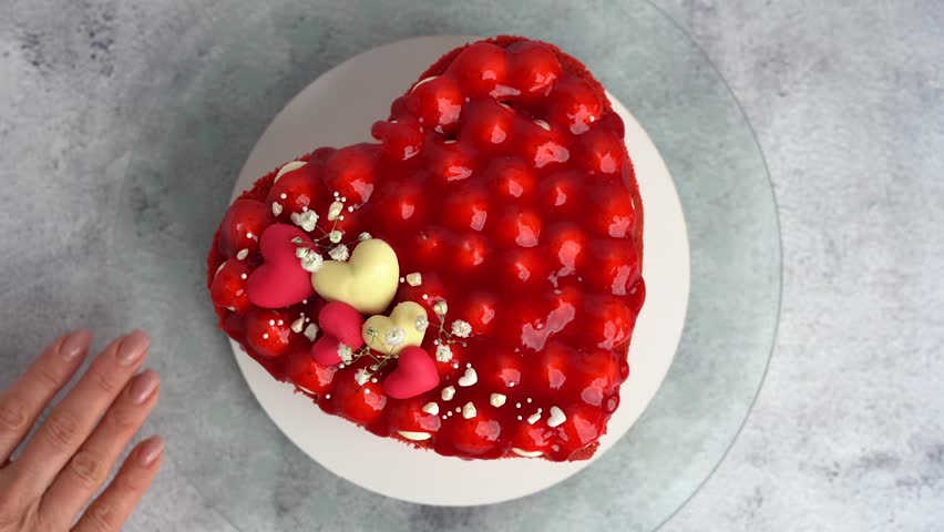 Beautiful red heart-shaped cake topped with strawberry jam on a gray background.