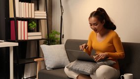 Young woman working on a laptop computer at the sofa, relaxing on a comfortable sofa. Happy life in the living room at home Home office work concept.