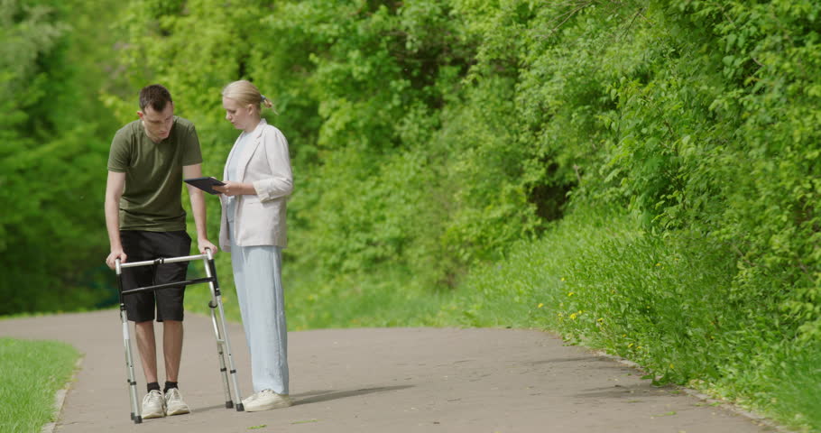 A health worker helps in the rehabilitation of a young man, teaches him to use a walker.