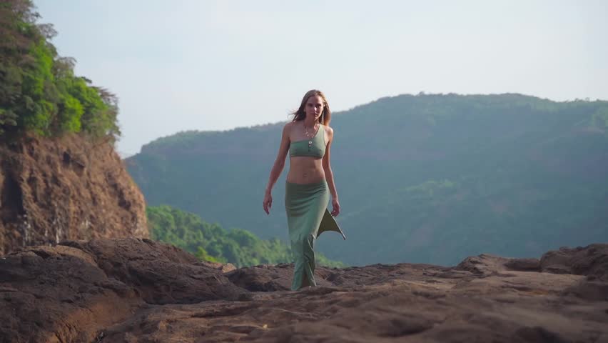 A girl in a dress sexually walks on the stones to meet the camera.