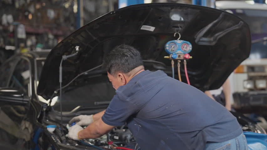 Back of Asian mechanic senior man or technician use tools to monitor pressure and gas of car engine and he also look to gauge to analysis and maintenance the car in garage.