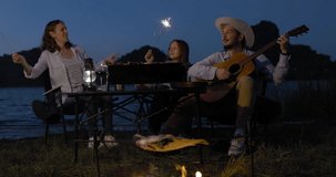 Happy family backpacker eat BBQ and drink and playing guitar together with happiness in Summer while having camping near lake at twilight time, 4k video