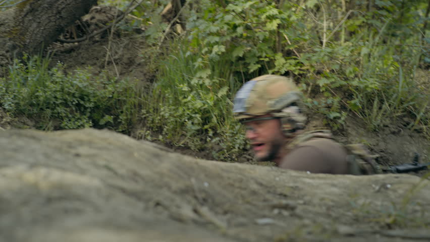Two male soldiers or warriors in camouflage uniform and helmets sneak up in trench and attack enemy positions firing from automatic rifles during assault. War or military conflict. Armed forces.