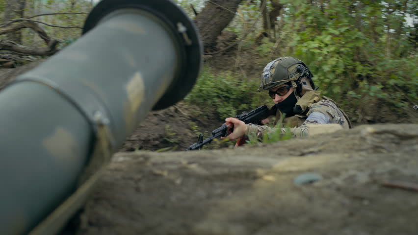 Two male soldiers or military men in camouflage uniform and helmets sneak up in trench and attack enemy positions shooting from automatic rifles. War or military conflict. Defense of the Homeland.