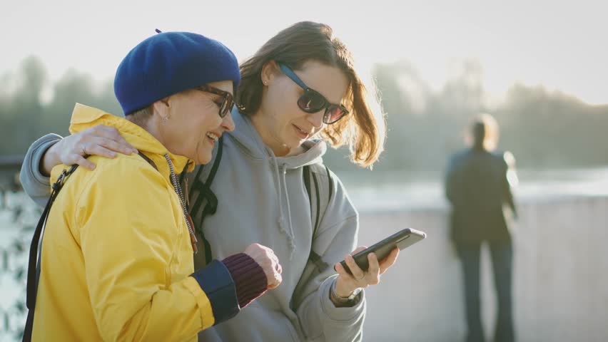 An adult granddaughter spends time with her cheerful grandmother walking and taking selfies on the phone.
