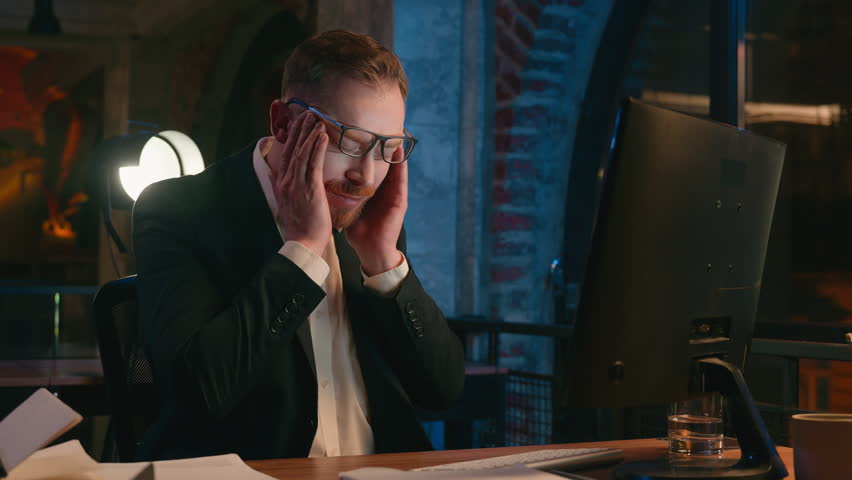 Caucasian businessman guy business man male worker working computer at night overtime office late time deadline feel headache pain head ache migraine tired exhausted fatigued overworked health problem