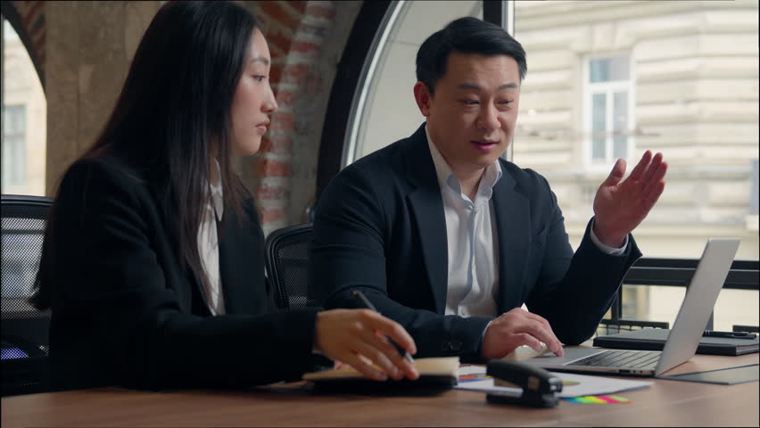 Two Asian business colleagues talking discuss online task computer work Korean man businessman teach using laptop corporate software Japanese Chinese businesswoman intern woman writing notes in office - Powered by Shutterstock - Get 15% off with code: PIKWIZARD15
