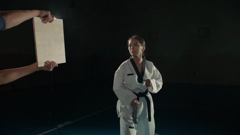Asian beautiful girl fighter practicing to break the board with a blow to the hand, taekwondo in slow motion