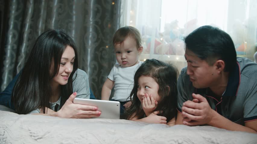 Asian couple with two children in their arms, happy family moments, have fun on the bed