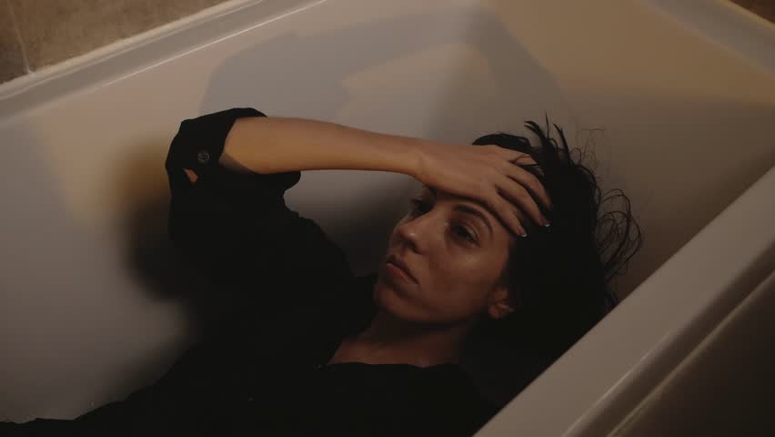 Melancholic woman submerged in bathtub, looking away