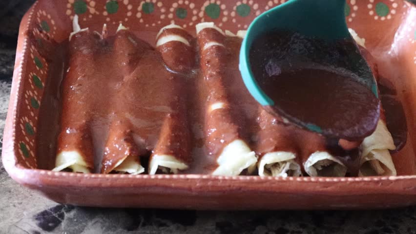 Slow motion still shot of spoon pouring mole sauce on tacos enchiladas. enmoladas mexican food