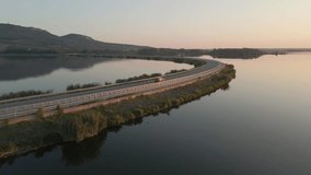 Drone video captures a scenic flight along a dam with traffic, flanked by lakes and the Pálava hills in the foreground.
