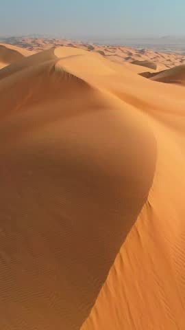 Flying over curve shaped sand dunes during hot summer weather. Rub' al Khali, aka Empty Quarter desert, Arabian Peninsula. Aerial vertical shot